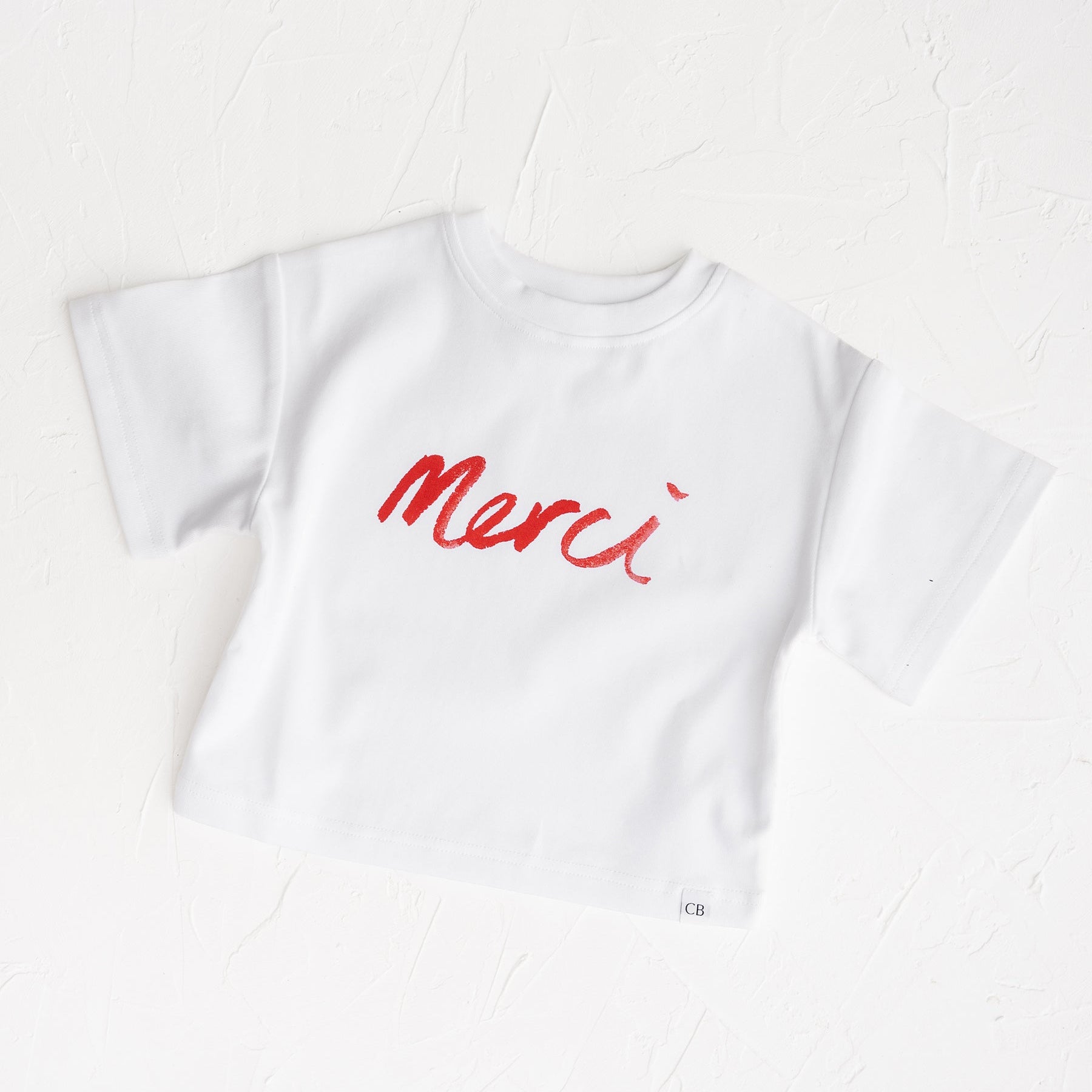 White t-shirt with red 'Merci' text on a white background Cinnamon Baby White Fox & Co exclusive 