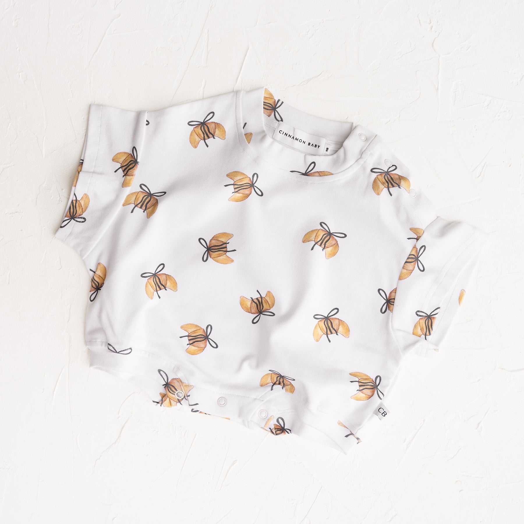 White baby t-shirt romper with crossiant pattern on a white background.  Cinnamon Baby Merci collection