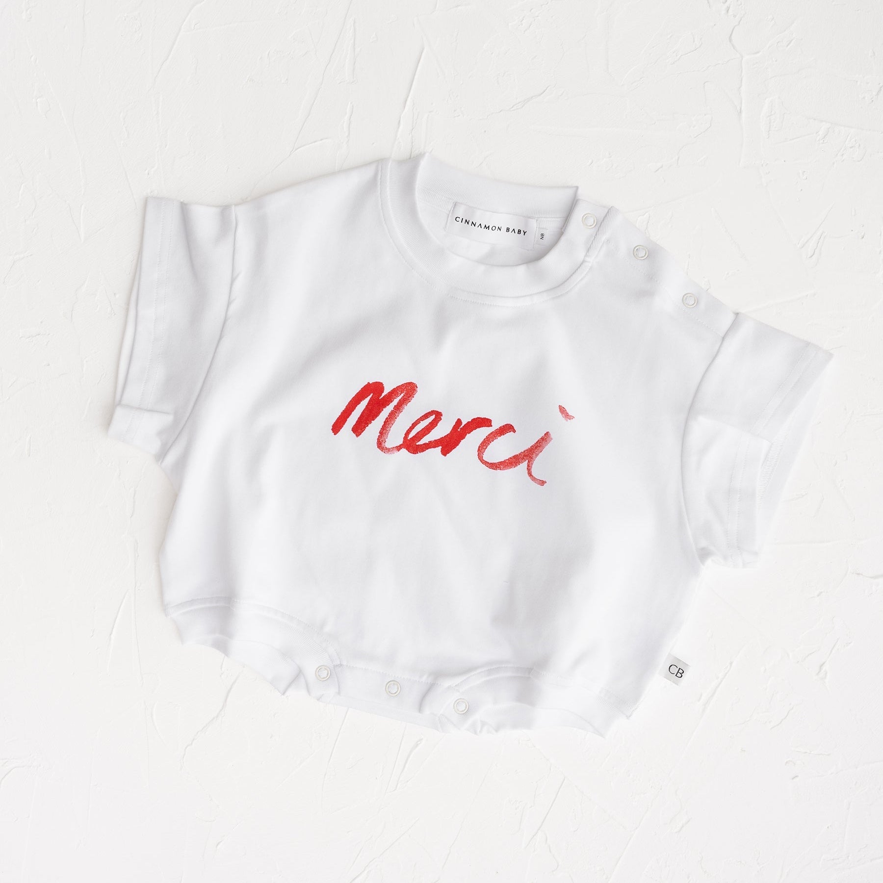 White t-shirt with red 'Merci' text on a white background, Merci collection by Cinnamon Baby exclusive to white Fox & Co