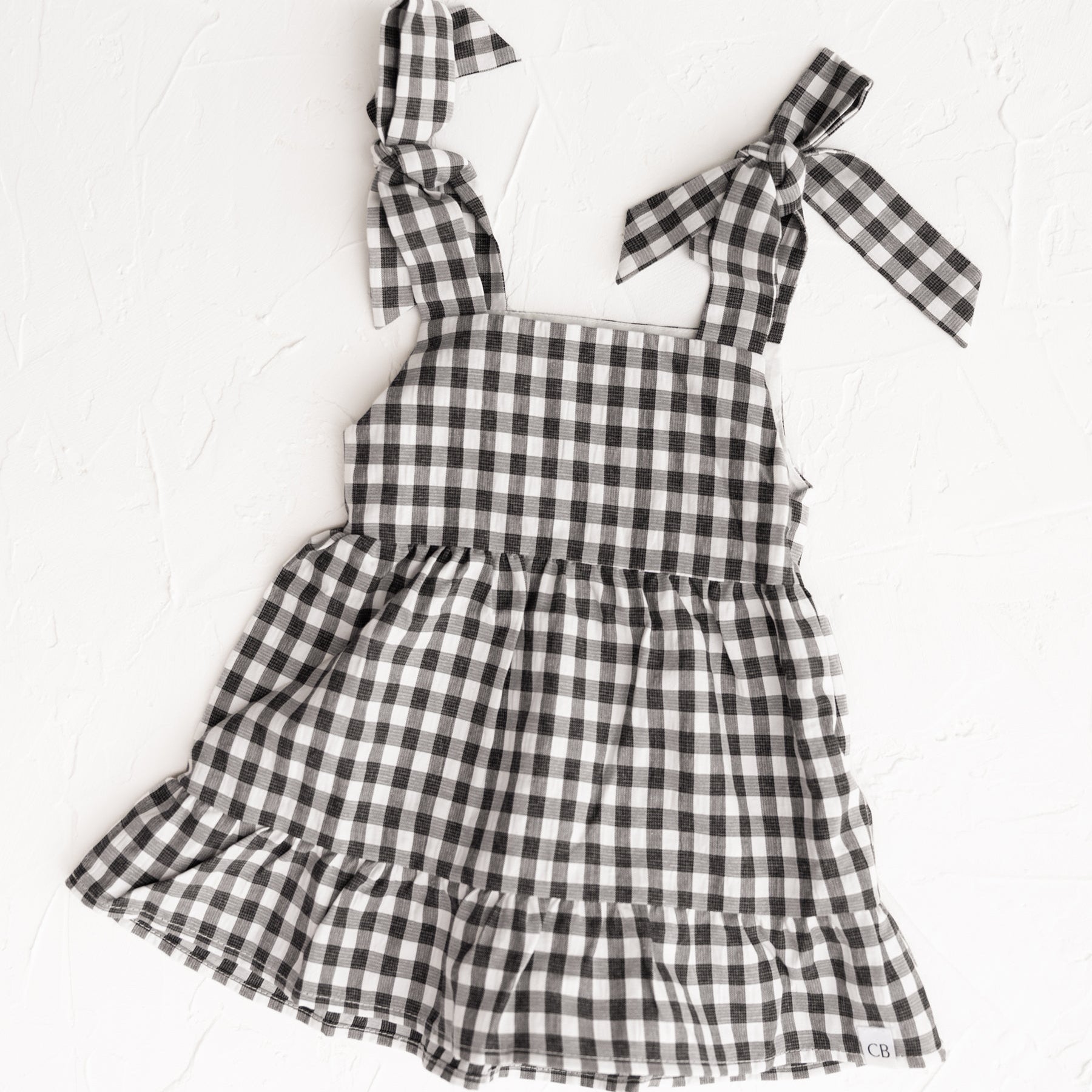 Cinnamon Baby Merci collection | Black and white checkered dress with bow straps on a white background
