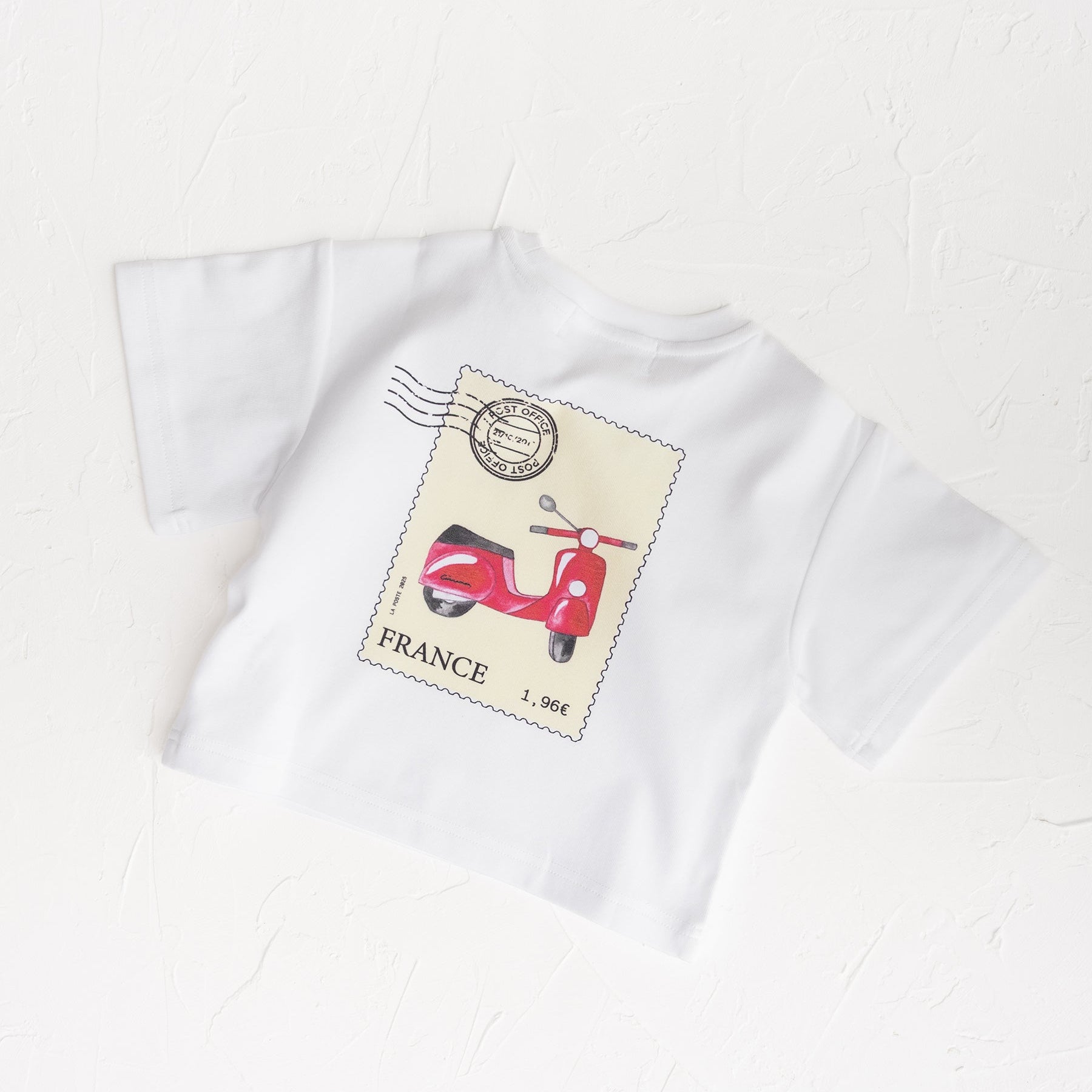 Cinnamon Baby Tee, postage stamp print, White shirt with a graphic of a red scooter on a beige background, resembling a vintage postcard, on a white background. White Fox & Co stockist 