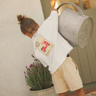 Cinnamon Baby Tee, postage stamp print, White shirt with a graphic of a red scooter on a beige background, resembling a vintage postcard, on a white background. White Fox & Co stockist 