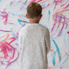 Child wearing a funfetti pullover sweater in surf standing in front of a colorful abstract wall.