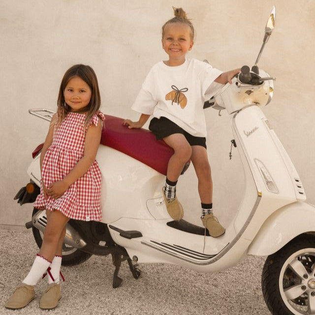 Two children sitting on a white scooter wearing Cinnamon Baby 