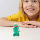 Child wearing a yellow shirt with a green toy dinosaur on a light background from hey clay monster set