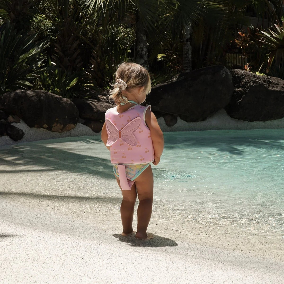 Child wearing Sunnylife Cotton Candy Cherry kids swim vest in the pool