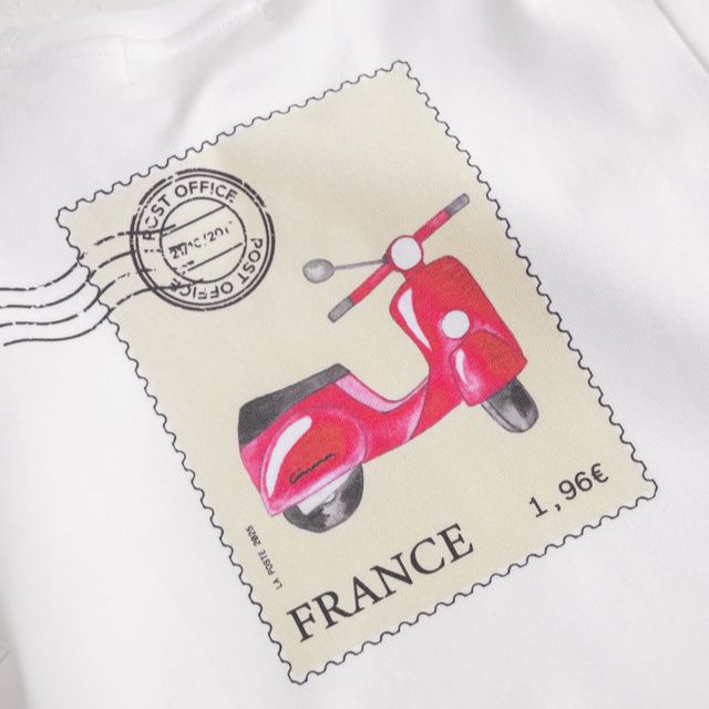 Cinnamon Baby Tee, postage stamp print, White shirt with a graphic of a red scooter on a beige background, resembling a vintage postcard, on a white background. White Fox & Co stockist 