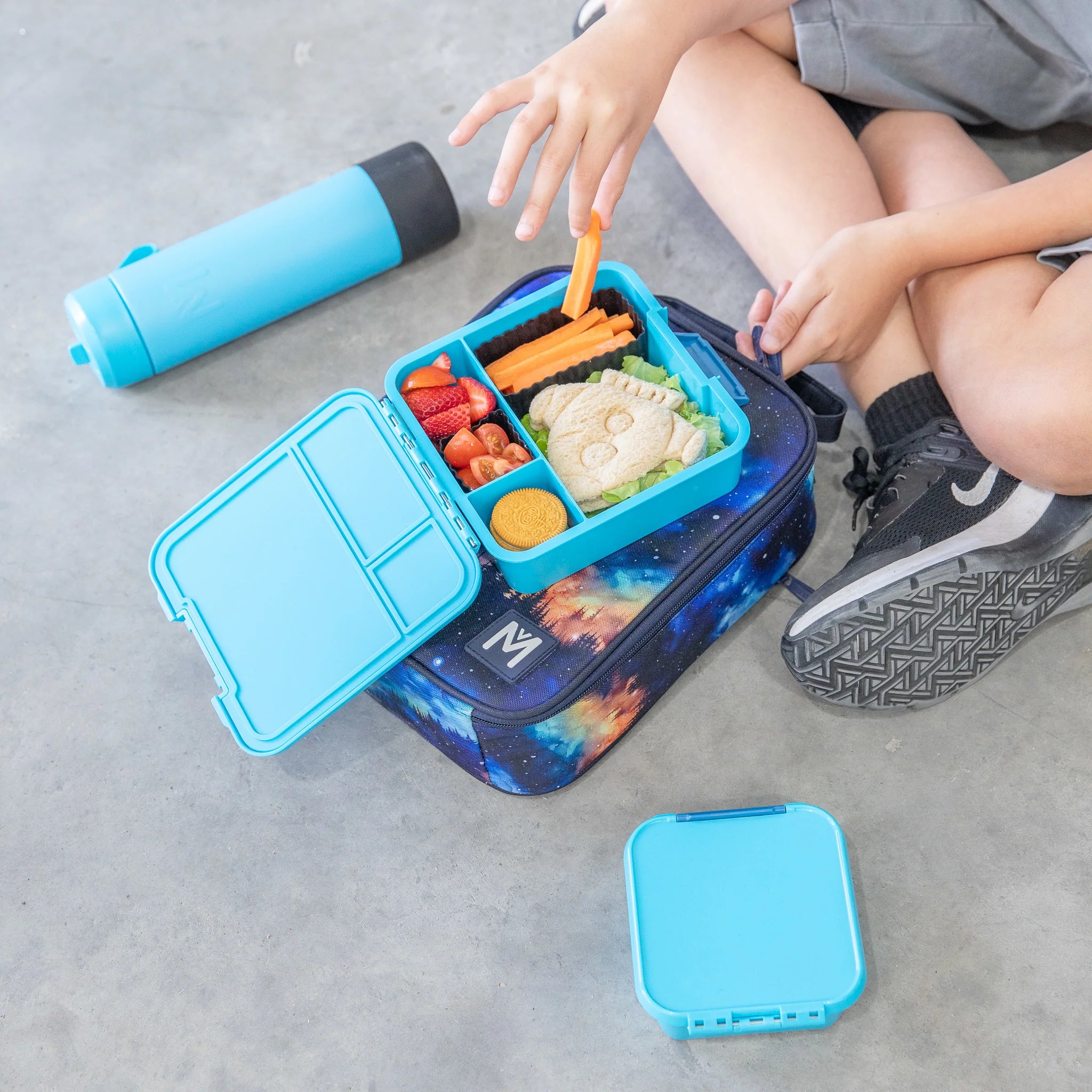 Child holding MontiiCo Bento Three in Coastal – blue lunchbox for school