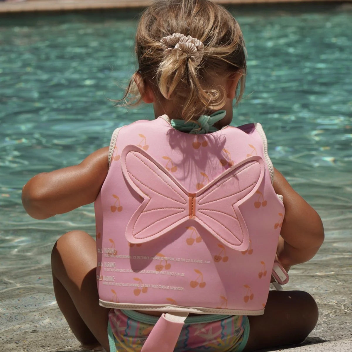 Child wearing Sunnylife Cotton Candy Cherry kids swim vest in the pool